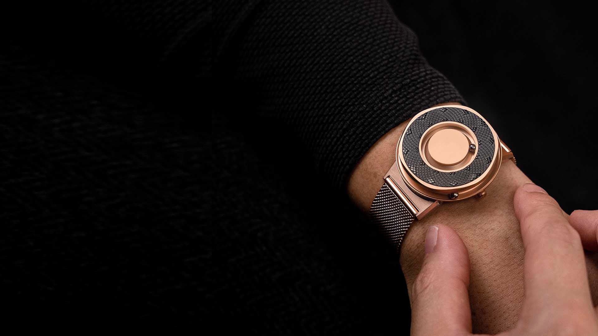 A wristshot of the Eone Rose Gold switch with a black sunflower ring attached. The timepiece is on a male wrist contrasted with a black sleeved top on a black dark background.