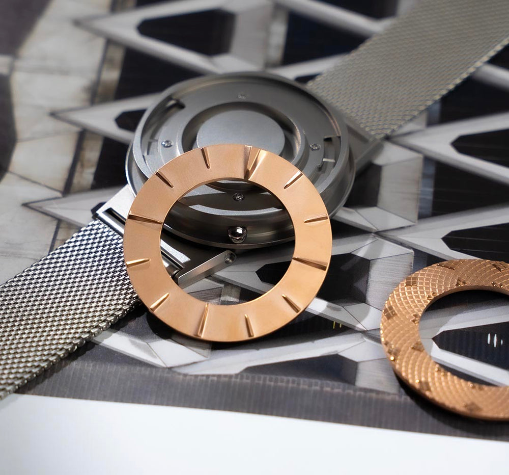 A disassembled Eone Switch Silver on top of a magazine. A rose gold 12 hour classic ring lays beside the timepiece.