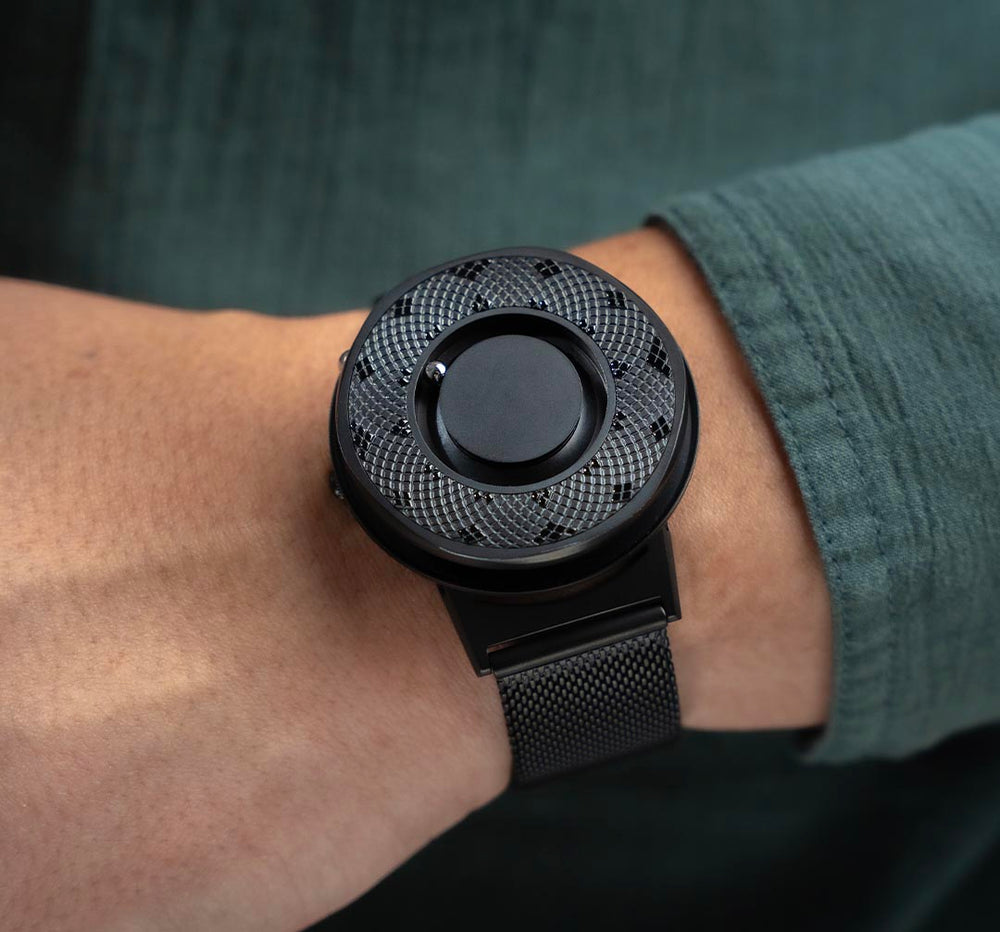 Shot at waist level and up close: A model wears the Eone Switch in black; fitted with the black sunflower ring. The model is dressed in a muted green linen shirt, providing a strong contrast for the timepiece to stand out.