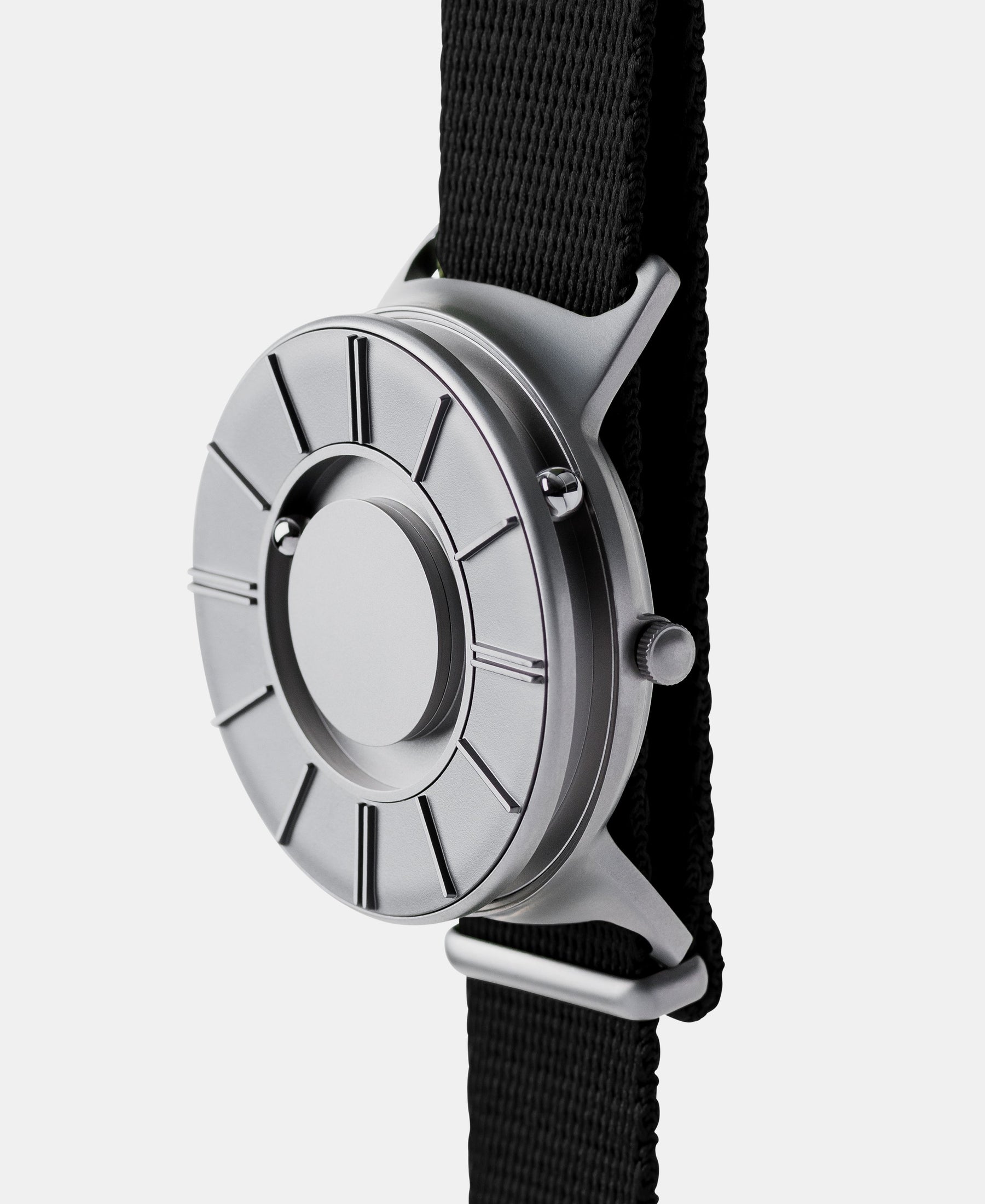 Load image into Gallery viewer, A photo of the watch from a side angle. The recessed track around the outside of the watch face is shown with the hour ball bearing in the track. The raised markers are noticeable from this perspective.