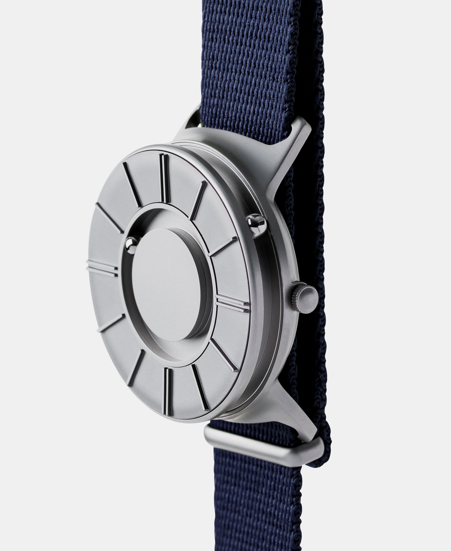 Load image into Gallery viewer, A photo of the watch from a side angle. The recessed track around the outside of the watch face is shown with the hour ball bearing in the track. The raised markers are noticeable from this perspective.