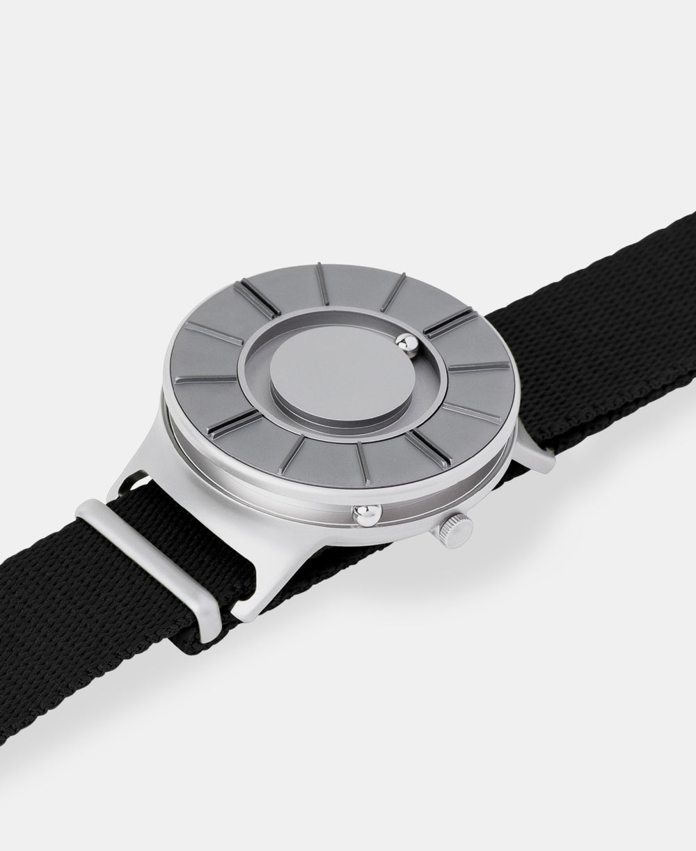 A photo of the watch lying flat on a surface. The recessed track around the outside of the watch face is shown with the hour ball bearing in the track. The raised markers are noticeable from this perspective.