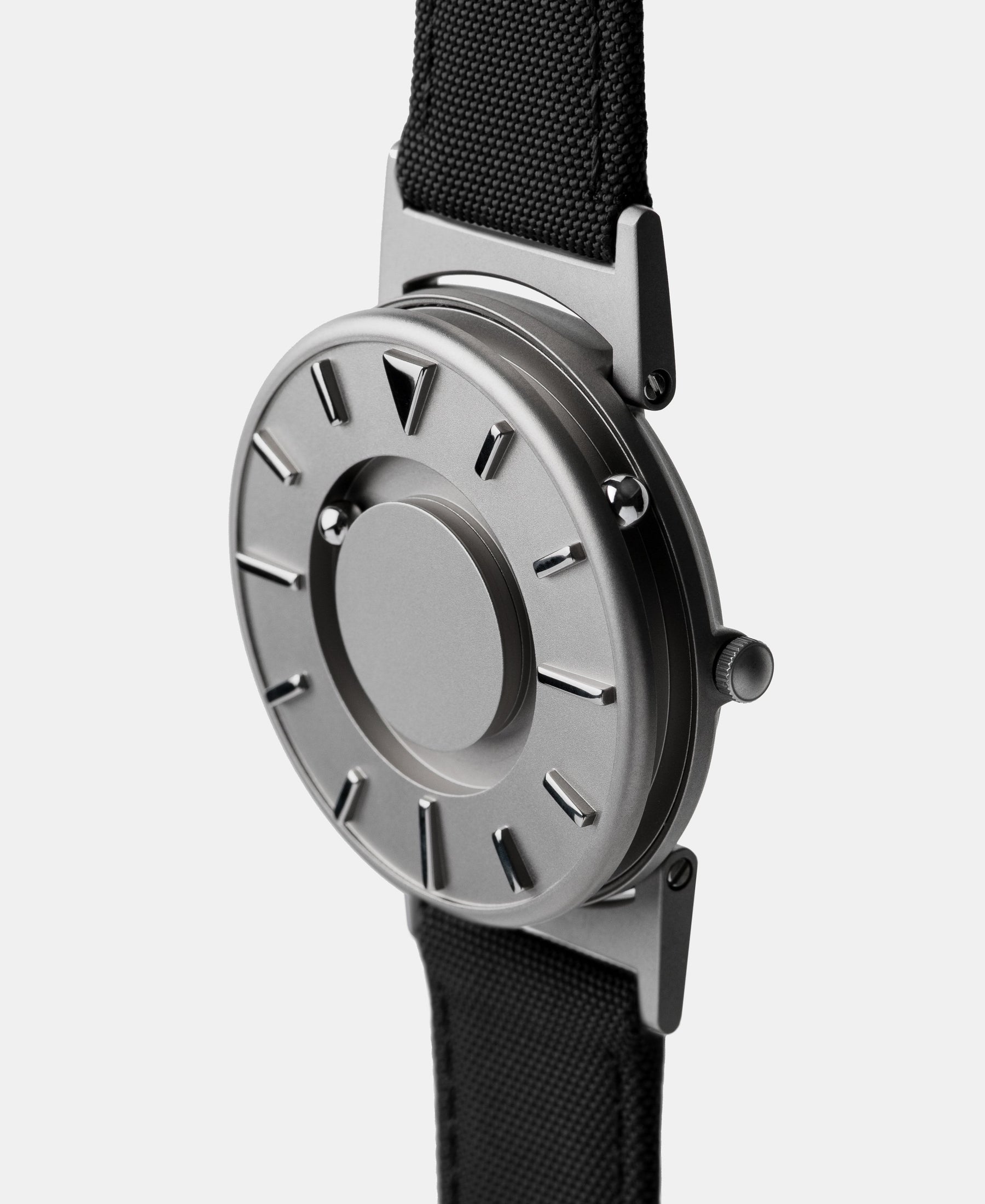 Load image into Gallery viewer, A photo of the watch from a side angle. The recessed track around the outside of the watch face is shown with the hour ball bearing in the track. The raised markers are noticeable from this perspective.