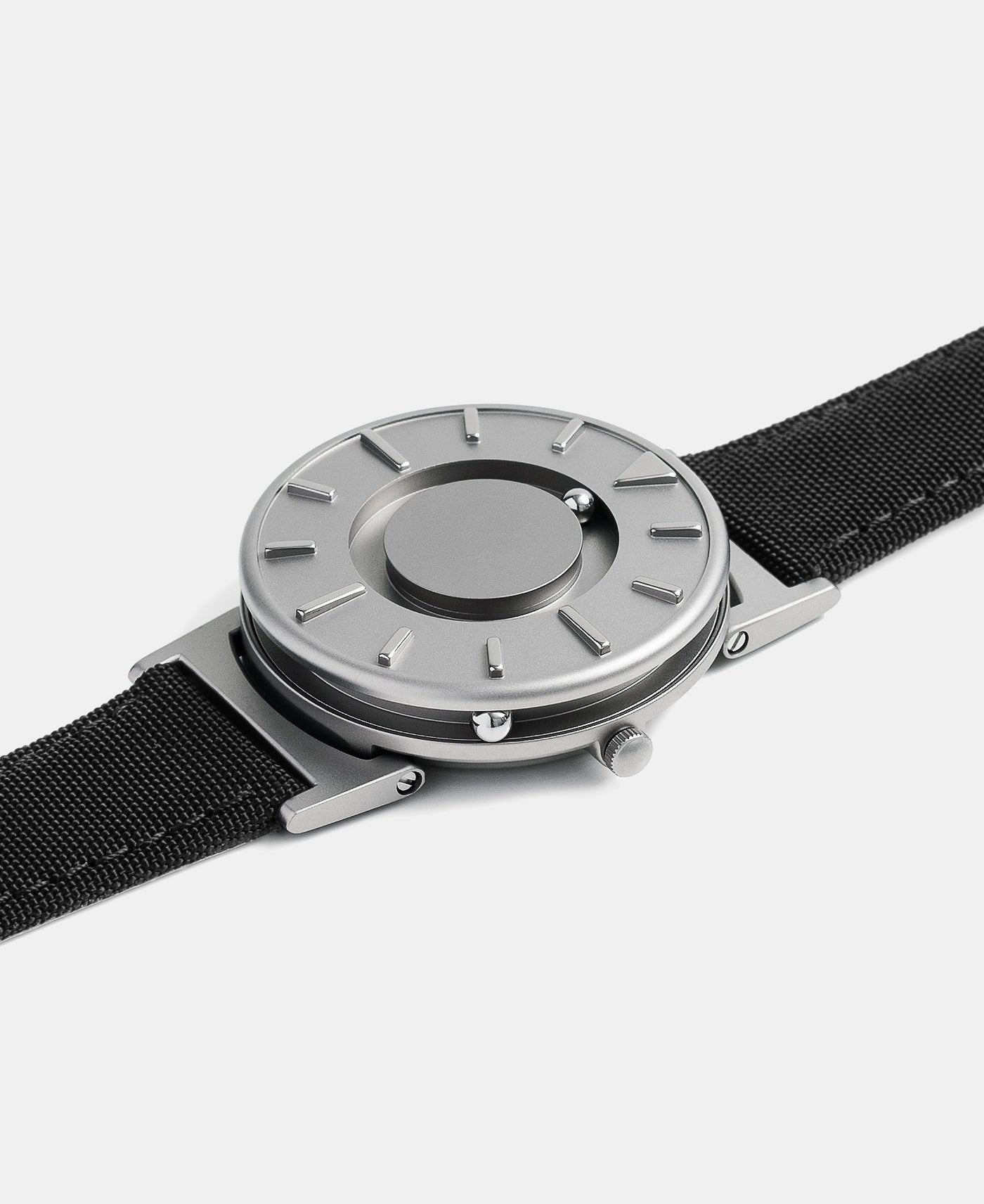 A photo of the watch lying flat on a surface. The recessed track around the outside of the watch face is shown with the hour ball bearing in the track. The raised markers are noticeable from this perspective.