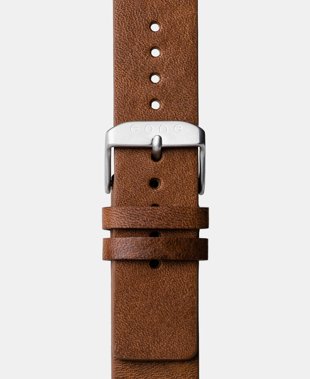 A photo shows the strap lying on a flat surface. One part has a buckle and the other part has a series of holes for an adjustable fit.